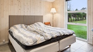 A bedroom with a large bed, a wooden headboard, a floor lamp, and a window with a view of a grassy area. - "Juste" - 1.7km from the sea by Interhome (Hals)