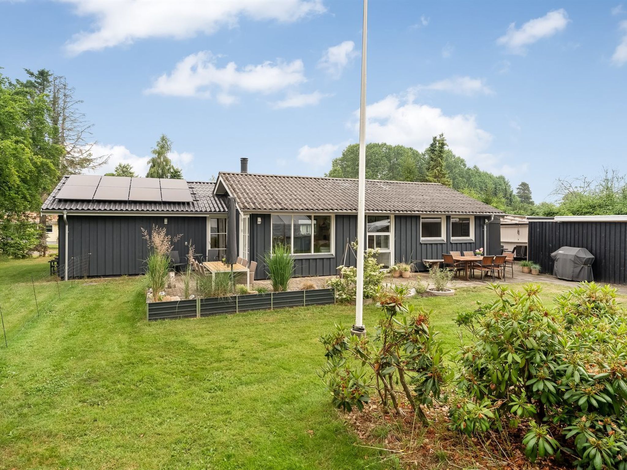A modern house with a large backyard, a patio with outdoor furniture, and a tall flagpole.
