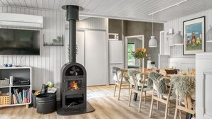 A modern living room with a wood-burning stove, a dining area with a wooden table and chairs, and a kitchen visible through an open door. - "Juste" - 1.7km from the sea by Interhome (Hals)