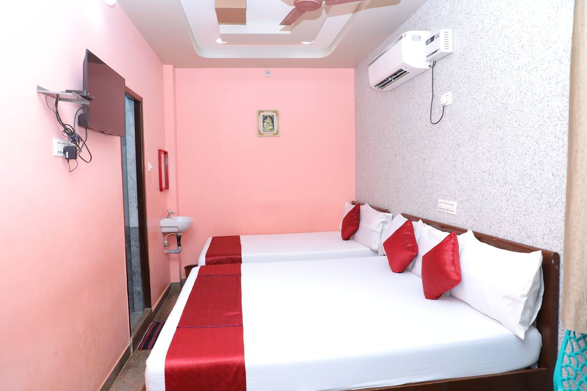 Habitación de hotel con dos camas, ventilador de techo, aire acondicionado, lavamanos y un cuadro en la pared.