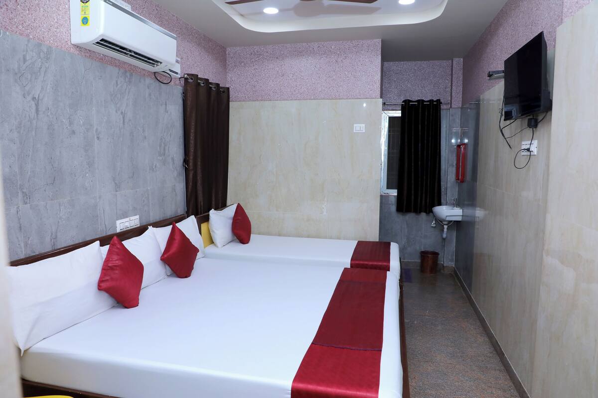 Habitación de hotel con cama, televisor montado en la pared y baño con lavamanos y ducha.