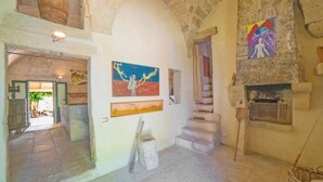 Un interno con pareti in pietra, una scala, un camino e opere d'arte alle pareti.