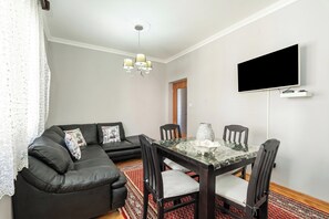 A living room with a black leather sofa, a glass-top dining table with chairs, a flat-screen TV mounted on the wall, and a patterned rug. - Seafront Haven Darka, Bijela, Montenegro (Bijela)
