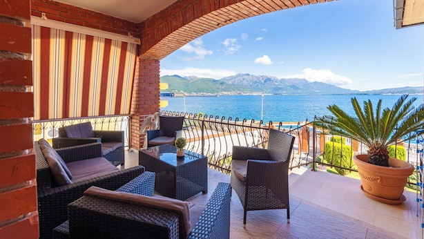 Ein Balkon mit Korbmöbeln, einer Topfpflanze und Blick auf das Meer und die Berge.