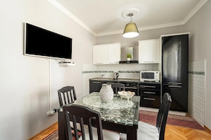 Uma cozinha compacta com televisão de tela plana, micro-ondas e área de refeições com mesa e cadeiras de vidro.