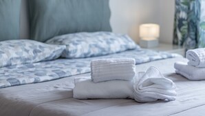 A neatly made bed with a patterned blue and white duvet, a stack of white towels, and a bedside lamp.