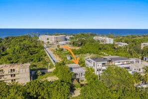 An aerial view of a coastal area with a hotel featuring a modern design, surrounded by lush greenery and a clear view of the ocean.