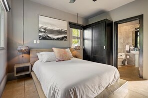 A modern bedroom with a large bed, bedside tables, a wall-mounted artwork, and a view into the bathroom.