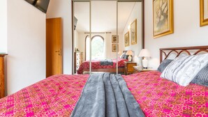 A bedroom with a large bed, a wardrobe, a mirror, and a door leading to a balcony. - Oleandro by Interhome (Villasimius)