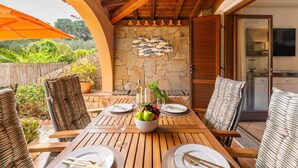An outdoor dining area with a stone wall, wooden ceiling, and a view of the garden. - Oleandro by Interhome (Villasimius)