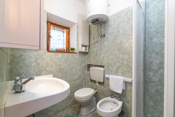 Un baño con lavabo, inodoro, bidé y una ventana con planta.