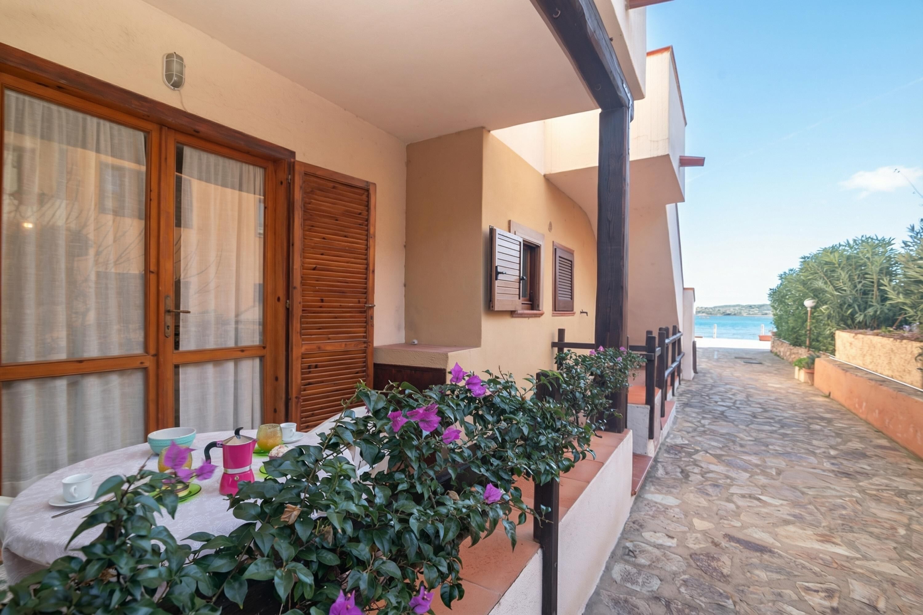 A balcony with a table set for dining, potted plants, and a view of the sea.
