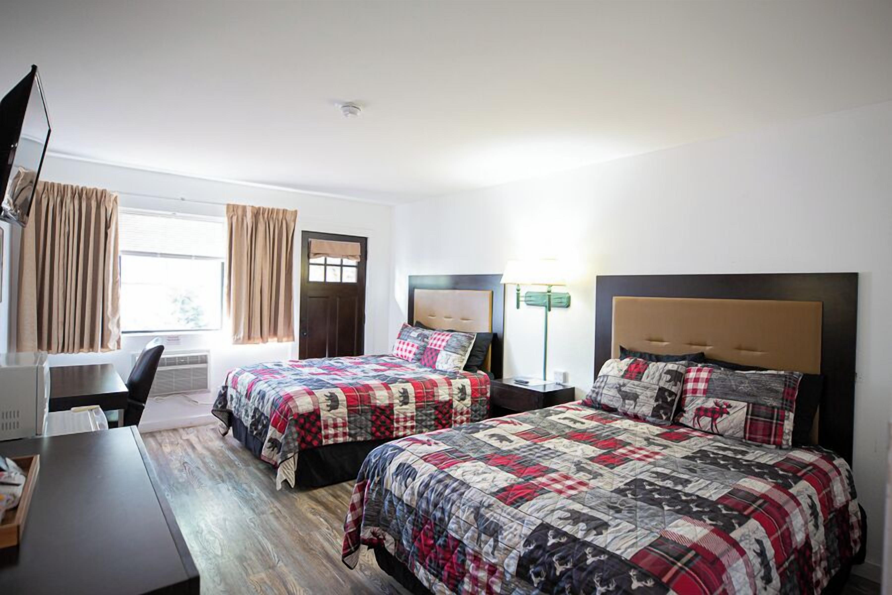 A hotel room with two beds, a desk, a chair, a lamp, and a window with curtains.