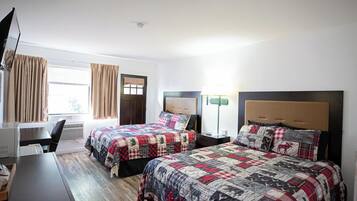 A hotel room with two beds, a desk, a chair, a lamp, and a window with curtains.