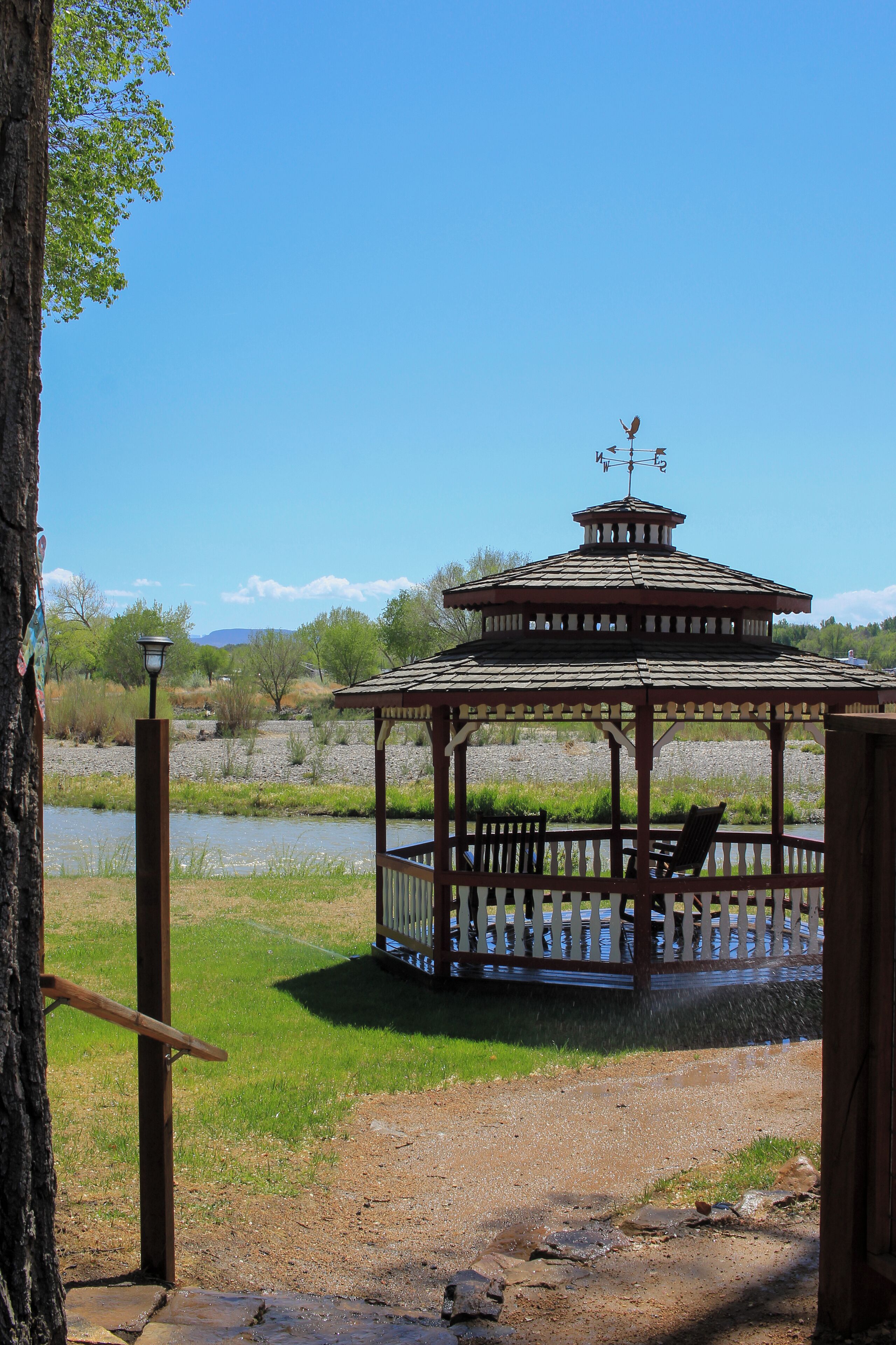 A gazebo with a bench, a lamp post, and a view of a river and mountains in the background.