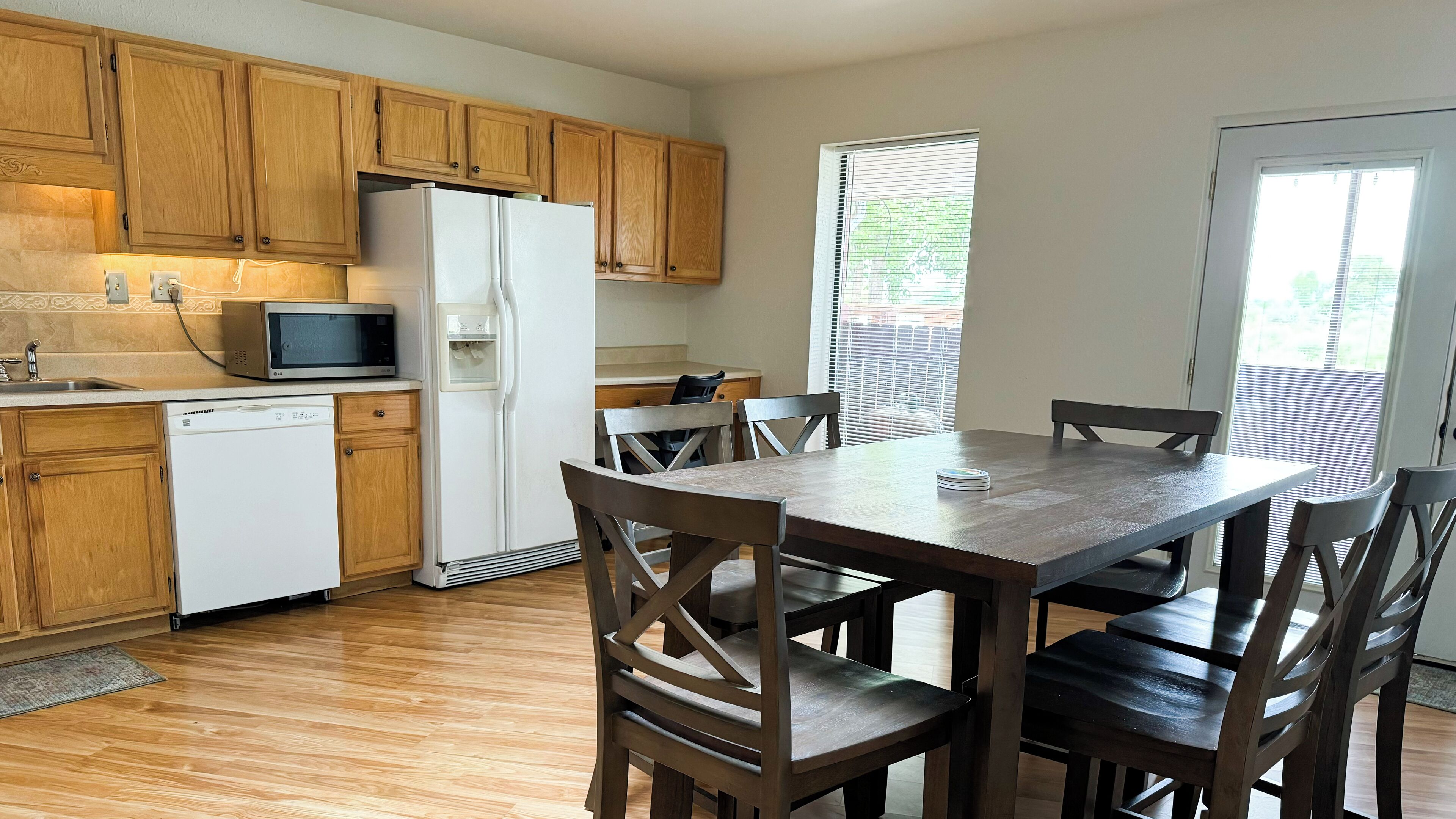A kitchen with wooden cabinets, a refrigerator, a microwave, and a dining table with chairs.