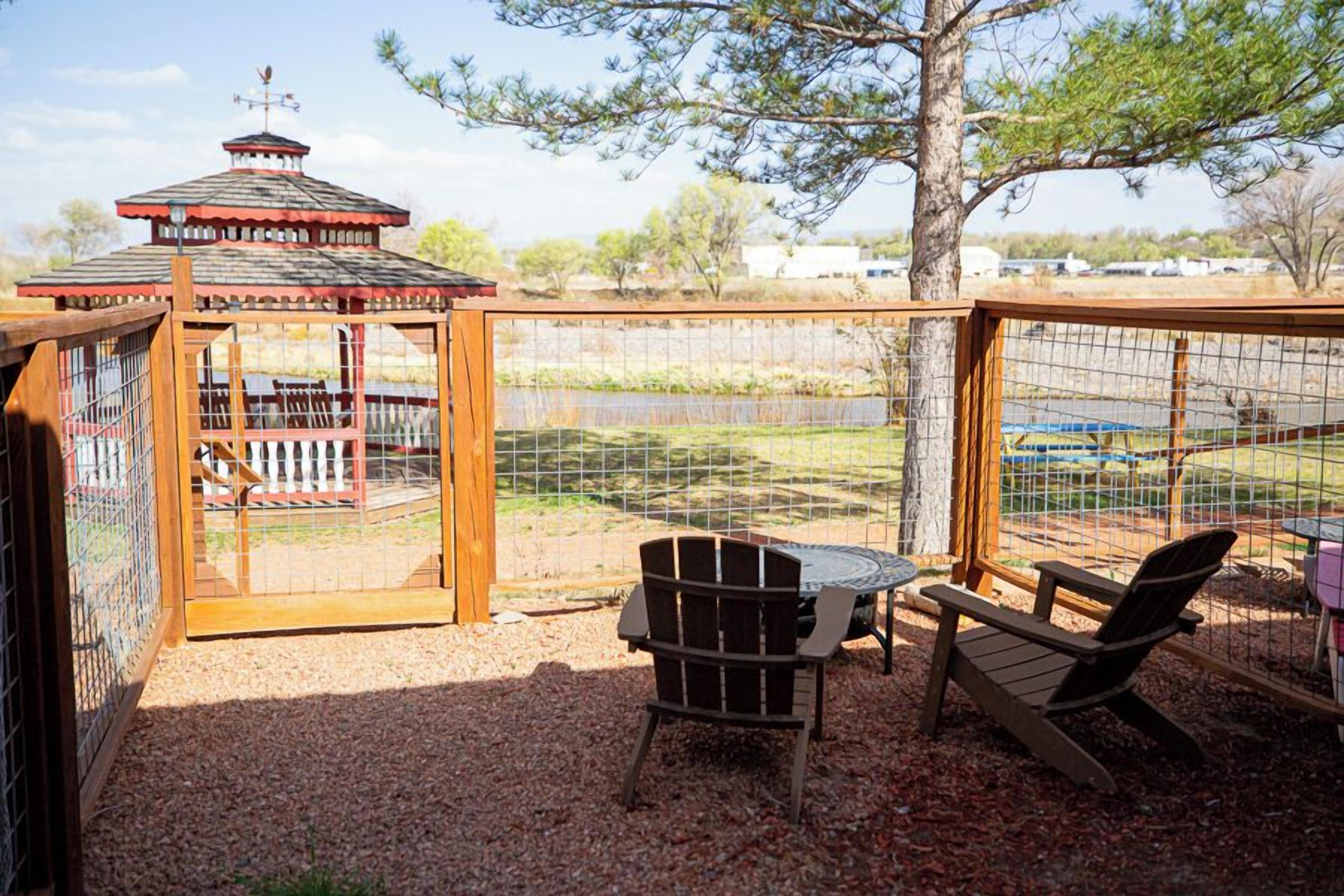 Un belvédère doté d’un toit en métal et d’une clôture en bois, qui entoure un espace patio aménagé avec deux fauteuils Adirondack et une petite table ronde.