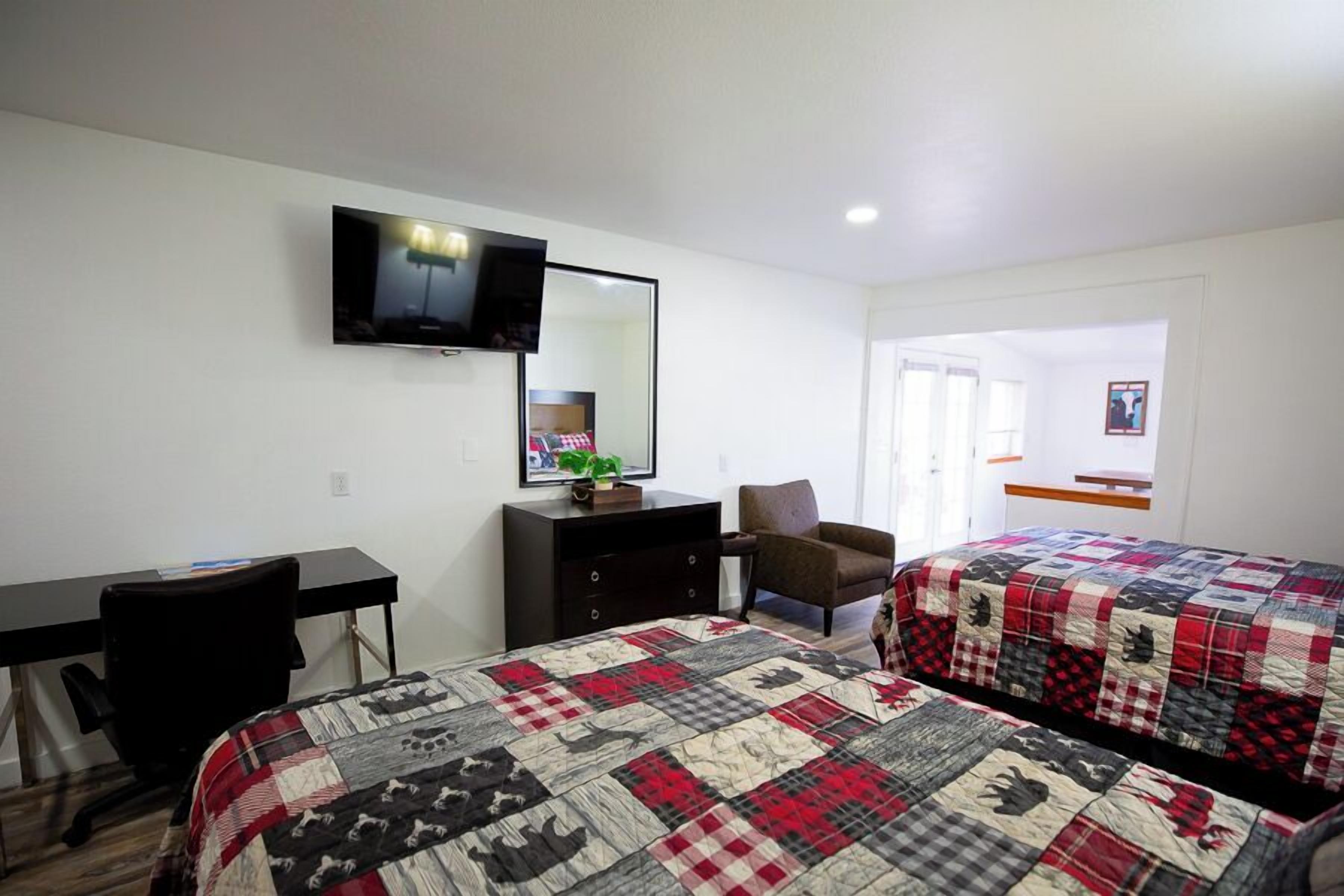Une chambre d’hôtel avec deux lits, un bureau, une chaise, une télévision et une commode.