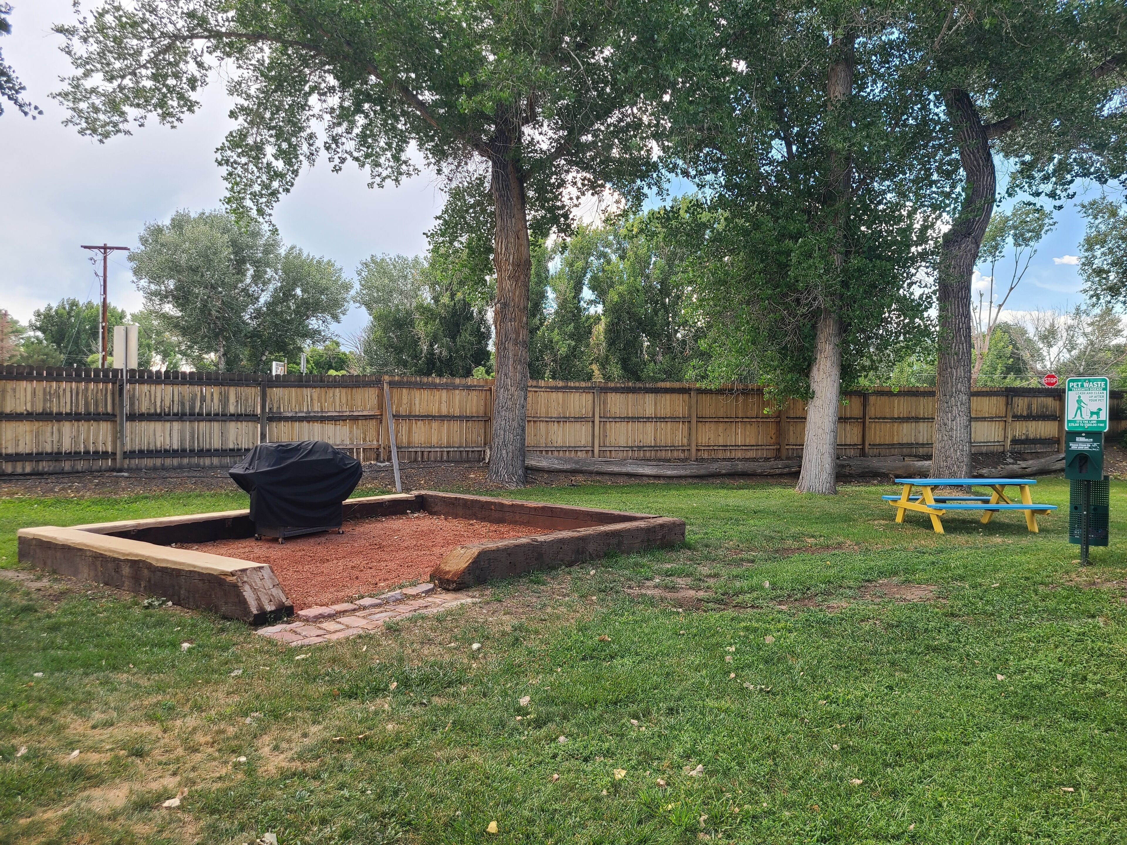 A backyard with a barbecue grill, picnic table, and a pet waste station.
