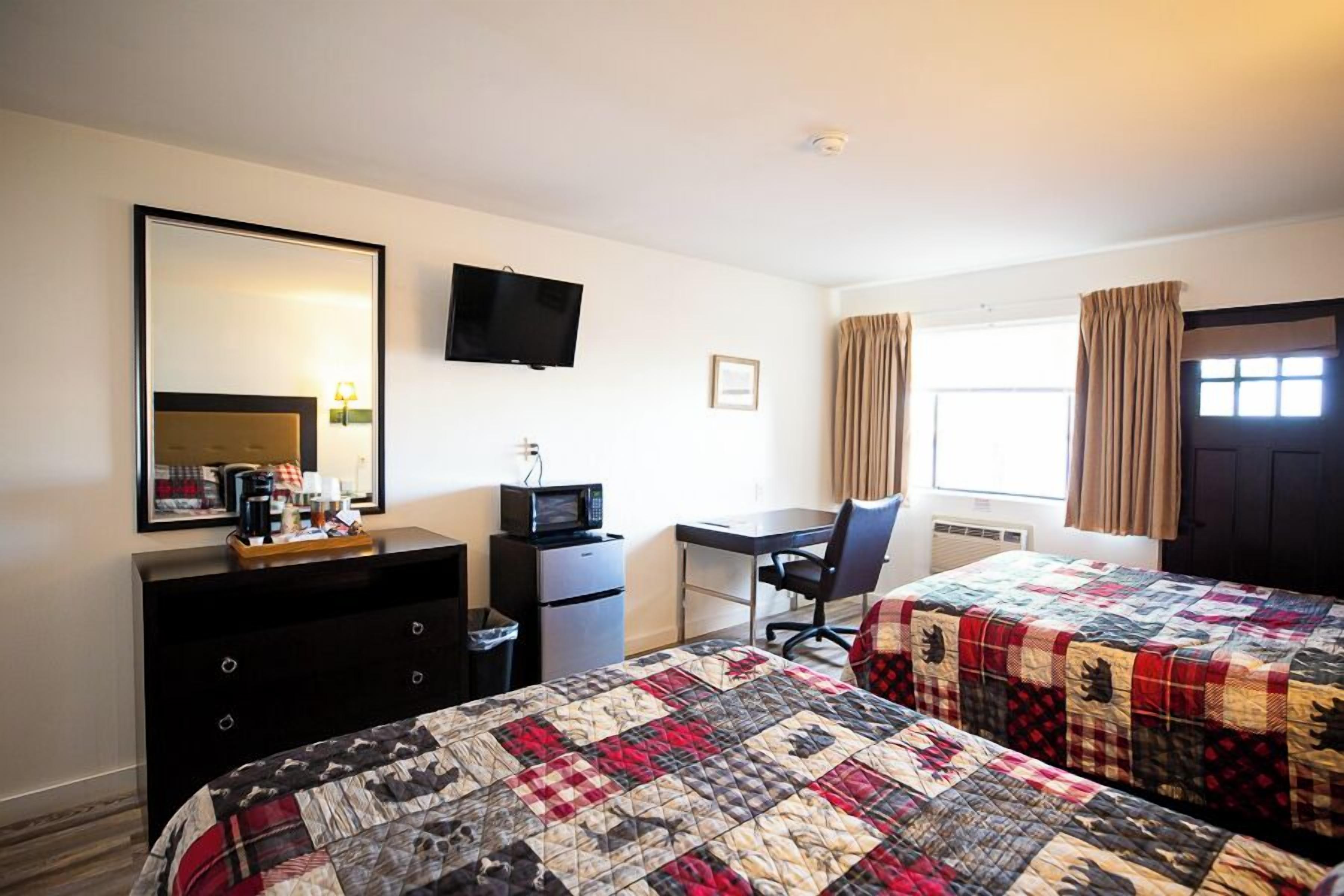 Een hotelkamer met twee bedden, een bureau, een televisie, een dressoir en een raam met gordijnen.