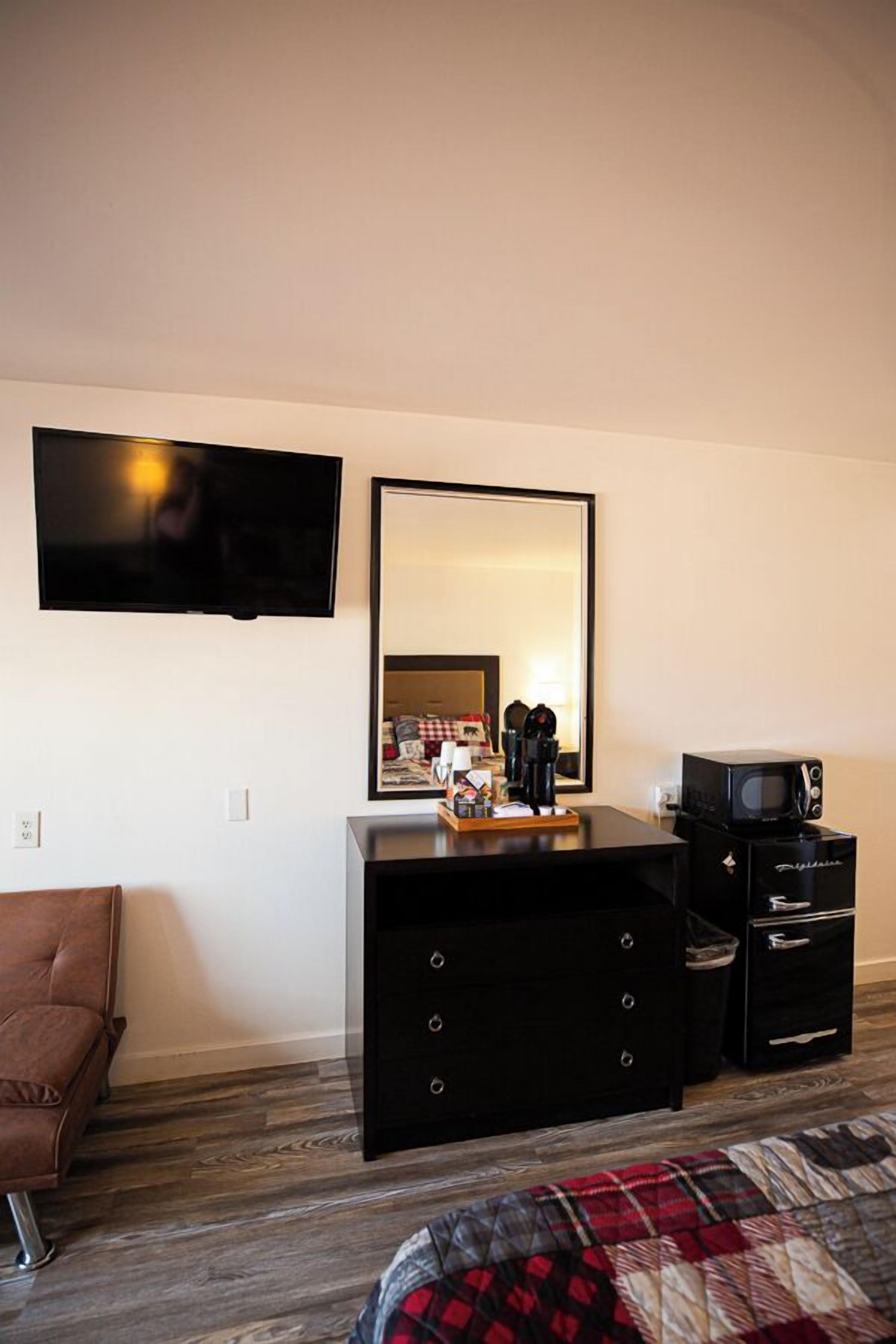 A hotel room with a flat-screen TV mounted on the wall, a large mirror above a dresser, and a microwave on the dresser.
