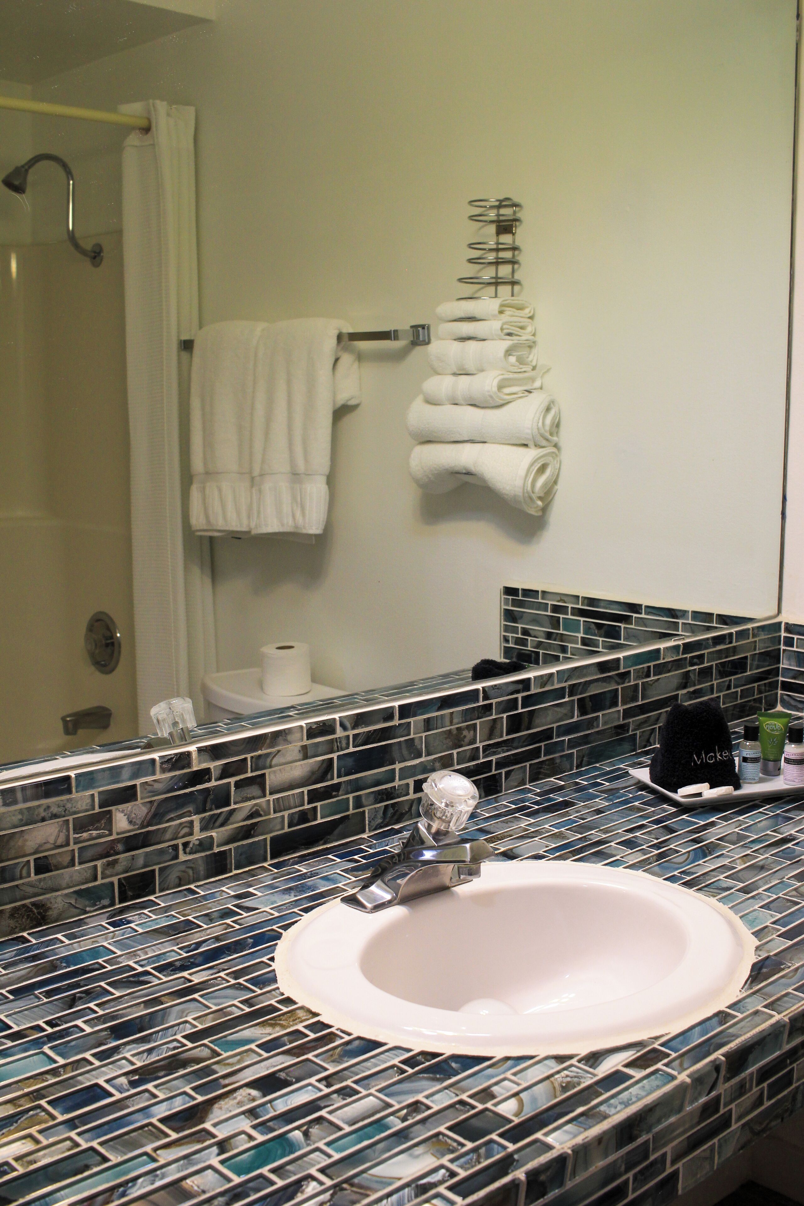 A bathroom with a tiled sink, a mirror, and a towel rack with folded towels.