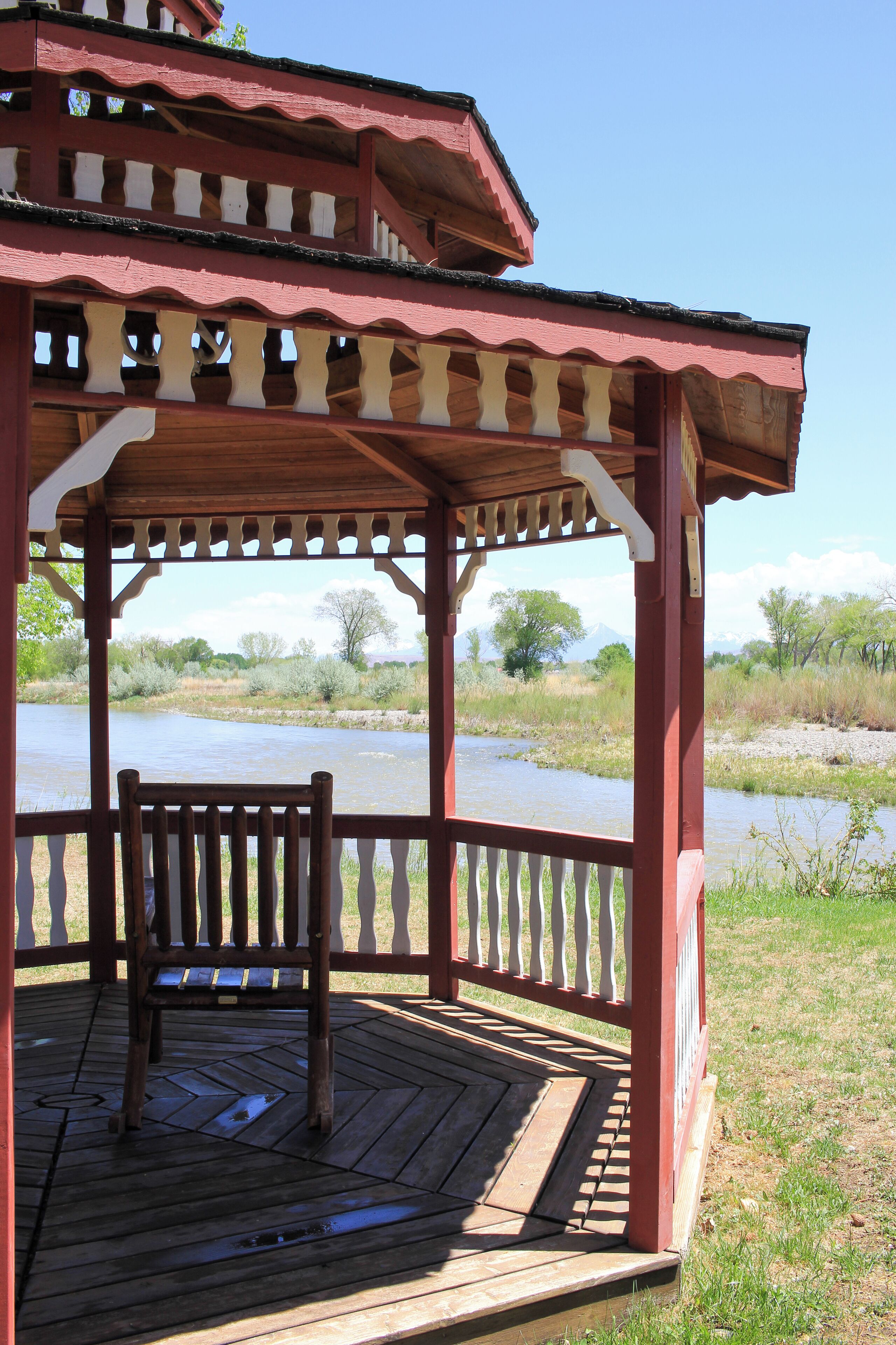 A wooden gazebo with a bench, overlooking a river.