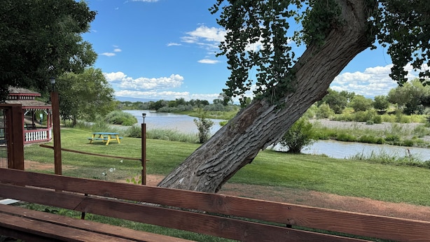 Een houten bank, een picknicktafel en een prieel aan een rivier.