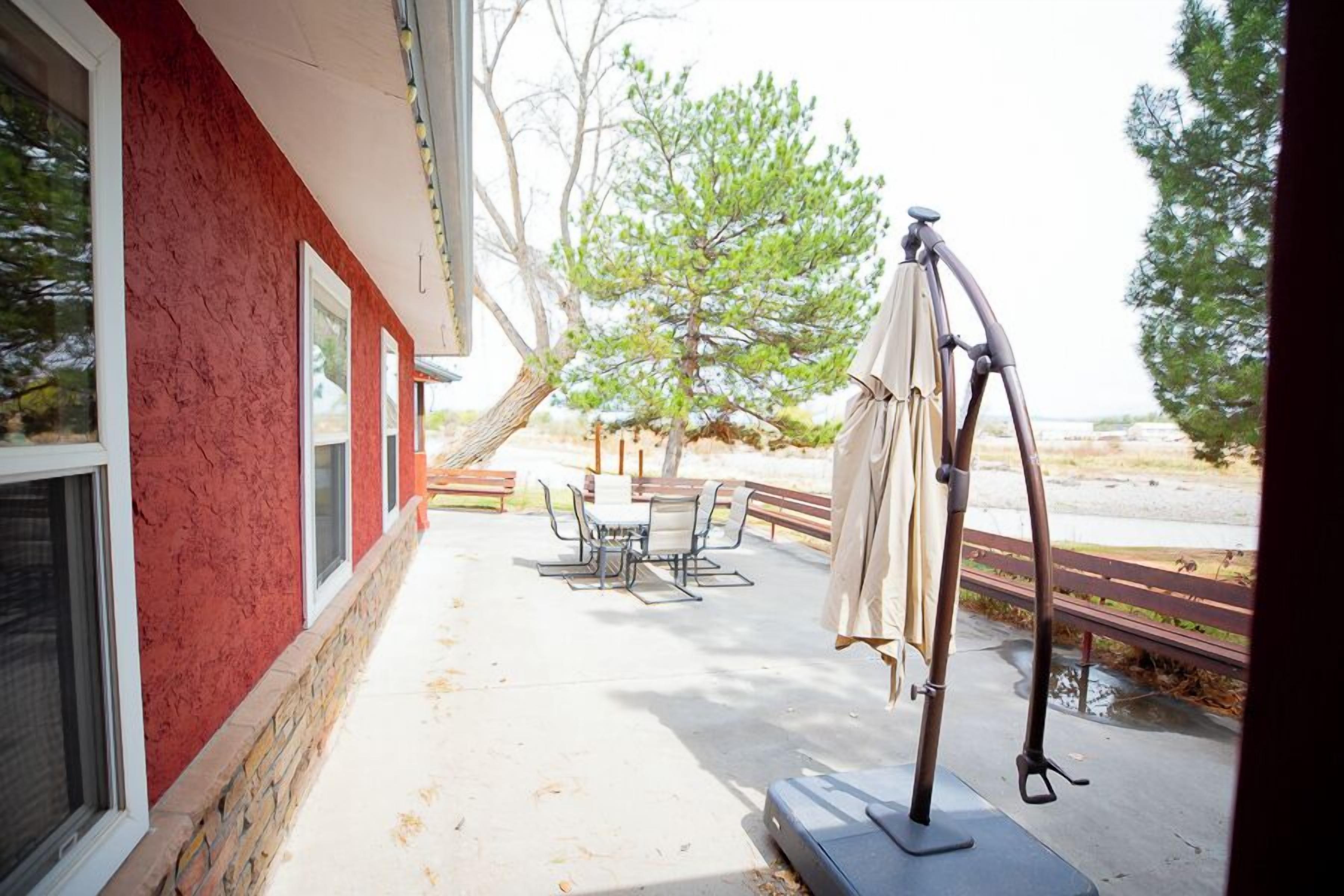 Un patio al aire libre con una mesa, sillas, una hamaca y una pérgola con sombrilla.