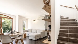 A modern living room with a sofa, dining table, chairs, and a staircase. - Vacation home Mela by Interhome (Porto Vecchio)