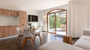 A modern kitchen with wooden cabinets, a dining area with white chairs, a flat-screen TV, and a sliding glass door leading to an outdoor patio. - Vacation home Mela by Interhome (Porto Vecchio)
