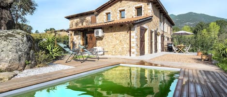 Una casa de piedra con piscina, mobiliario exterior y vistas a la montaña.