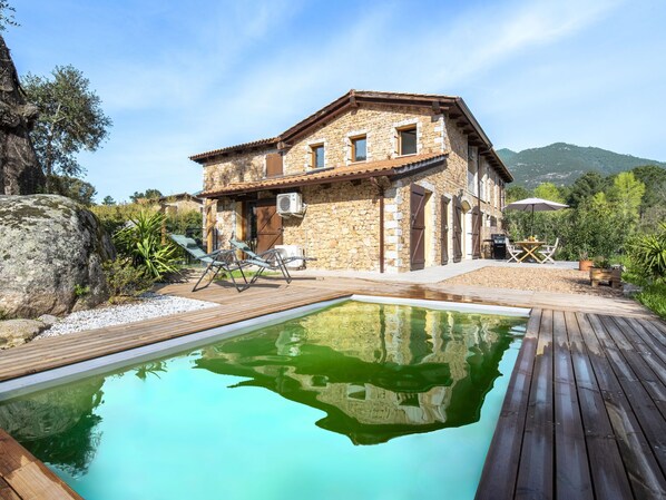 A stone house with a swimming pool, outdoor furniture, and a view of the mountains.