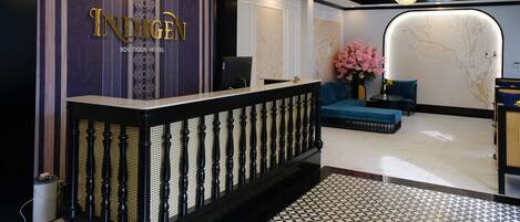 A hotel reception area with a reception desk, a chandelier, a sofa, and a decorative wall.