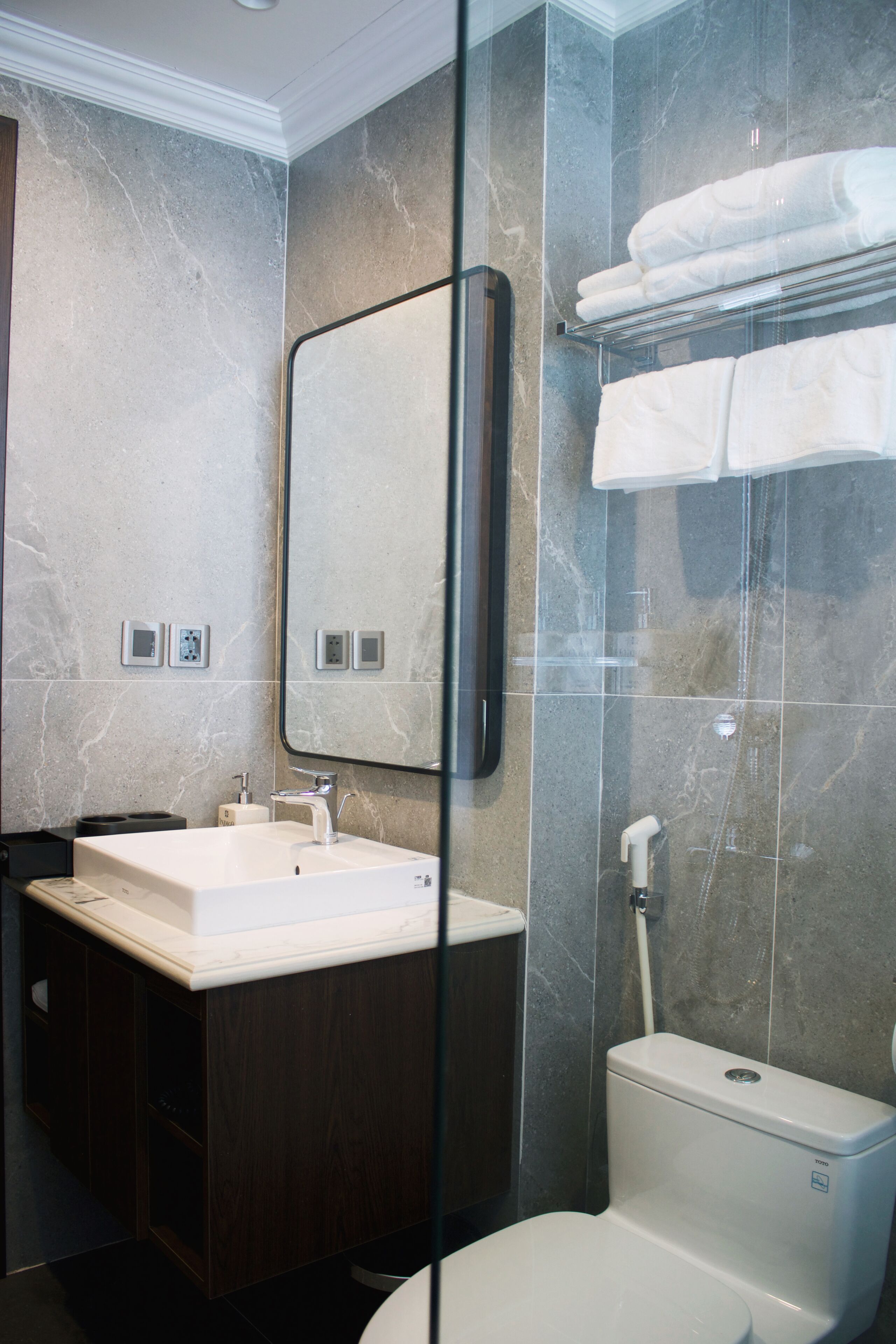 A modern bathroom with a marble wall, a glass shower enclosure, a white sink, and a toilet.
