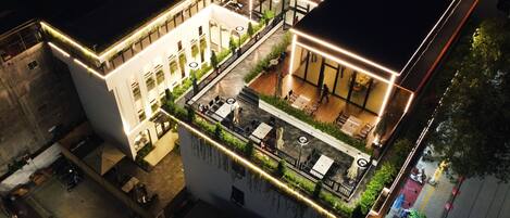 An aerial view of a modern building with multiple floors, outdoor seating areas, and a rooftop terrace.