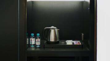 A minibar with snacks, bottled water, a kettle, and a refrigerator displaying beverages.