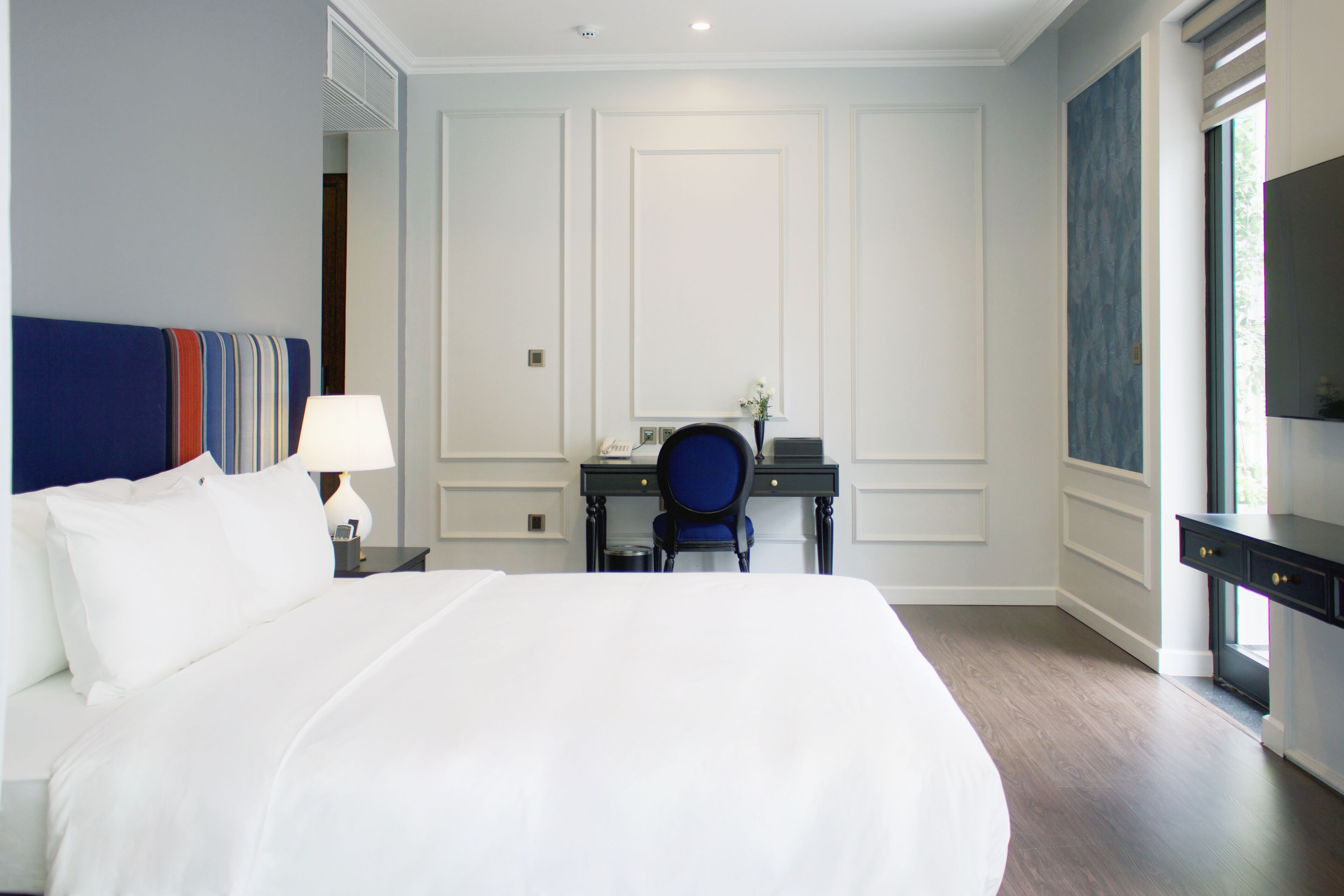 A hotel room with a large bed, a desk with a chair, a lamp, and a TV on a stand.