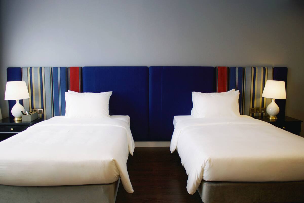 A hotel room with two beds, a blue headboard, and bedside lamps.