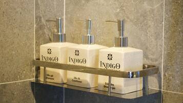 Une étagère de salle de bain avec trois bouteilles blanches étiquetées « Indigo » et « Dâu gói Shampoo » (shampoing), « Dâu Xá Conditioner » (après-shampoing) et « Sữa rửa gel » (gel douche).