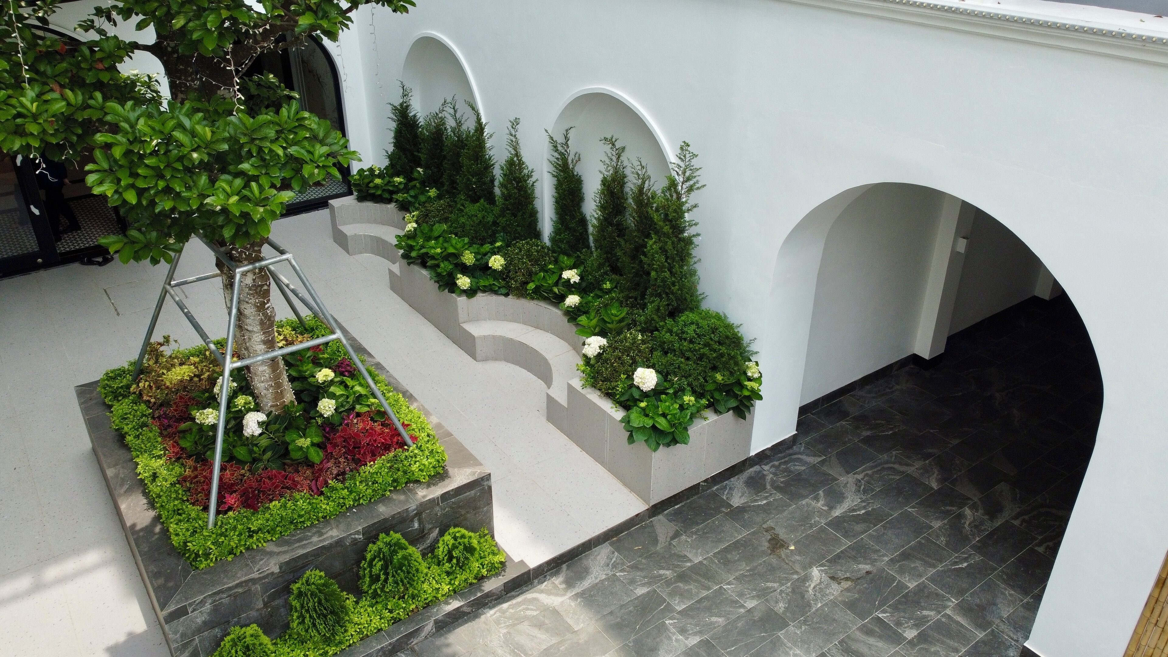 Un patio exterior con jardín central, escalones de piedra y paredes blancas con arcos.