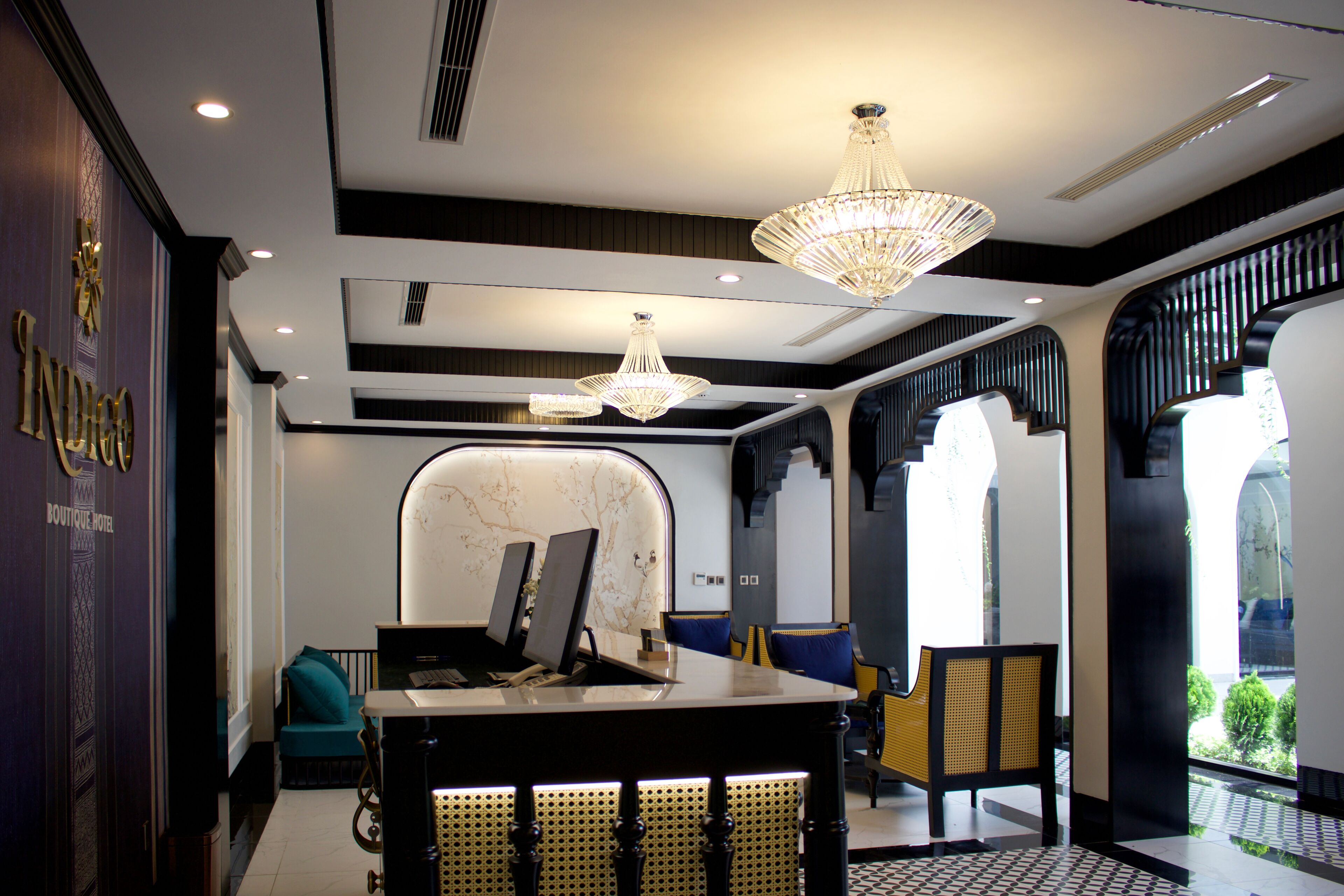 A modern hotel lobby with a reception desk, seating area, and a chandelier.