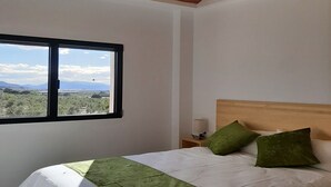 Ein Schlafzimmer mit einem Bett, einem Nachttisch, einer Lampe und einem Fenster mit Blick auf die Landschaft.