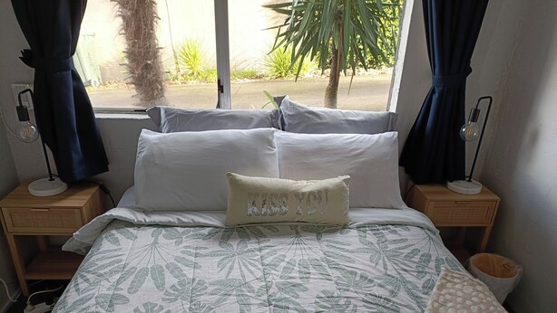 A neatly made bed with a leaf-patterned bedspread, a pillow with "KISS YOU" text, and a bedside lamp on each side. - 1970's Retro style 2 bed unit (Auckland)