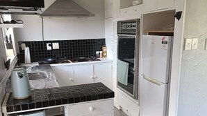A modern kitchen with white cabinets, a black countertop, a stove, and a refrigerator. - 1970's Retro style 2 bed unit (Auckland)