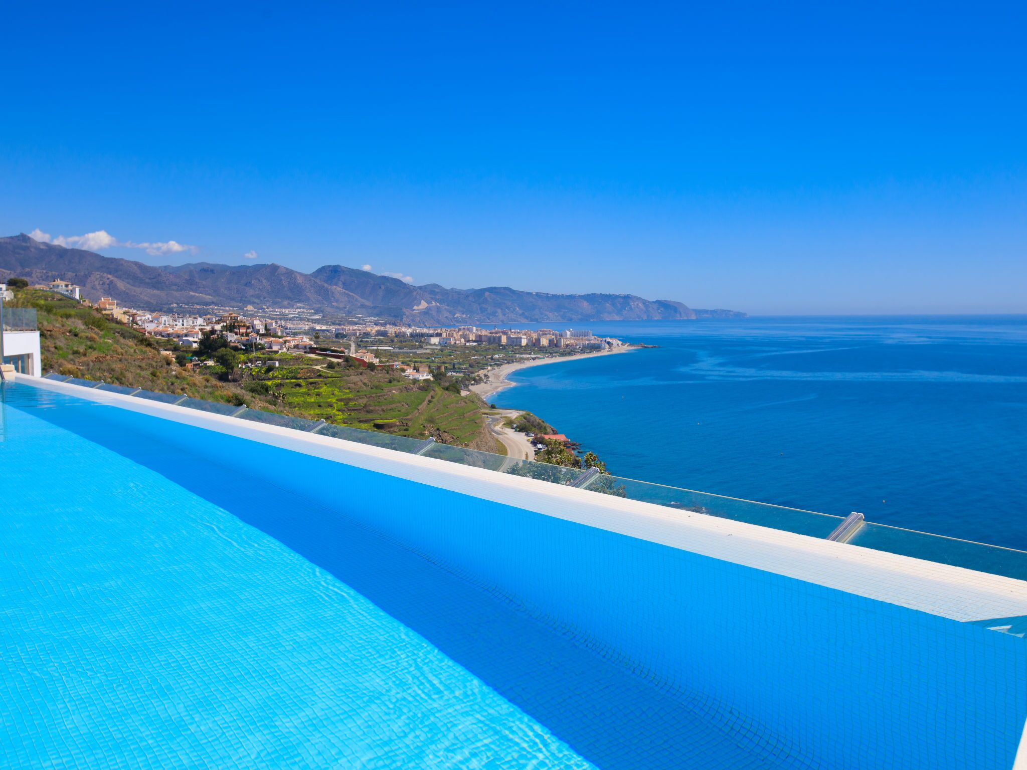 Une piscine avec vue sur une ville côtière et les montagnes.