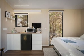 Une chambre moderne équipée d’un lit, d’un bureau intégré avec un micro-ondes, d’un petit lavabo et d’une fenêtre donnant sur des arbres.