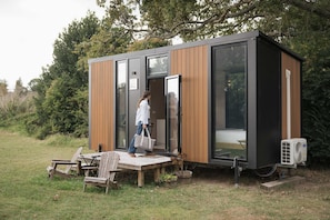 A modern cabin with a sliding door, a small outdoor seating area, and an air conditioning unit. - Sweet Hart 2 by Tiny Away (Tamahere)
