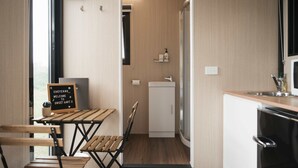 A compact kitchen with a wooden table and chairs, a refrigerator, a sink, and a shower area.