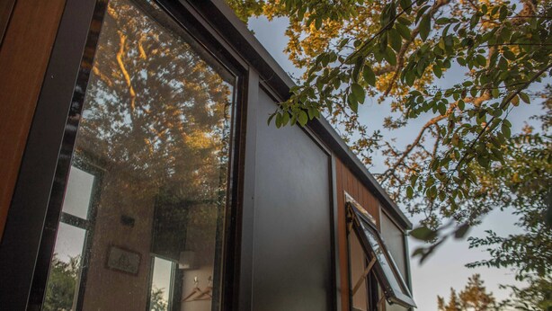 A modern building with large windows, a wooden exterior, and a view of trees.